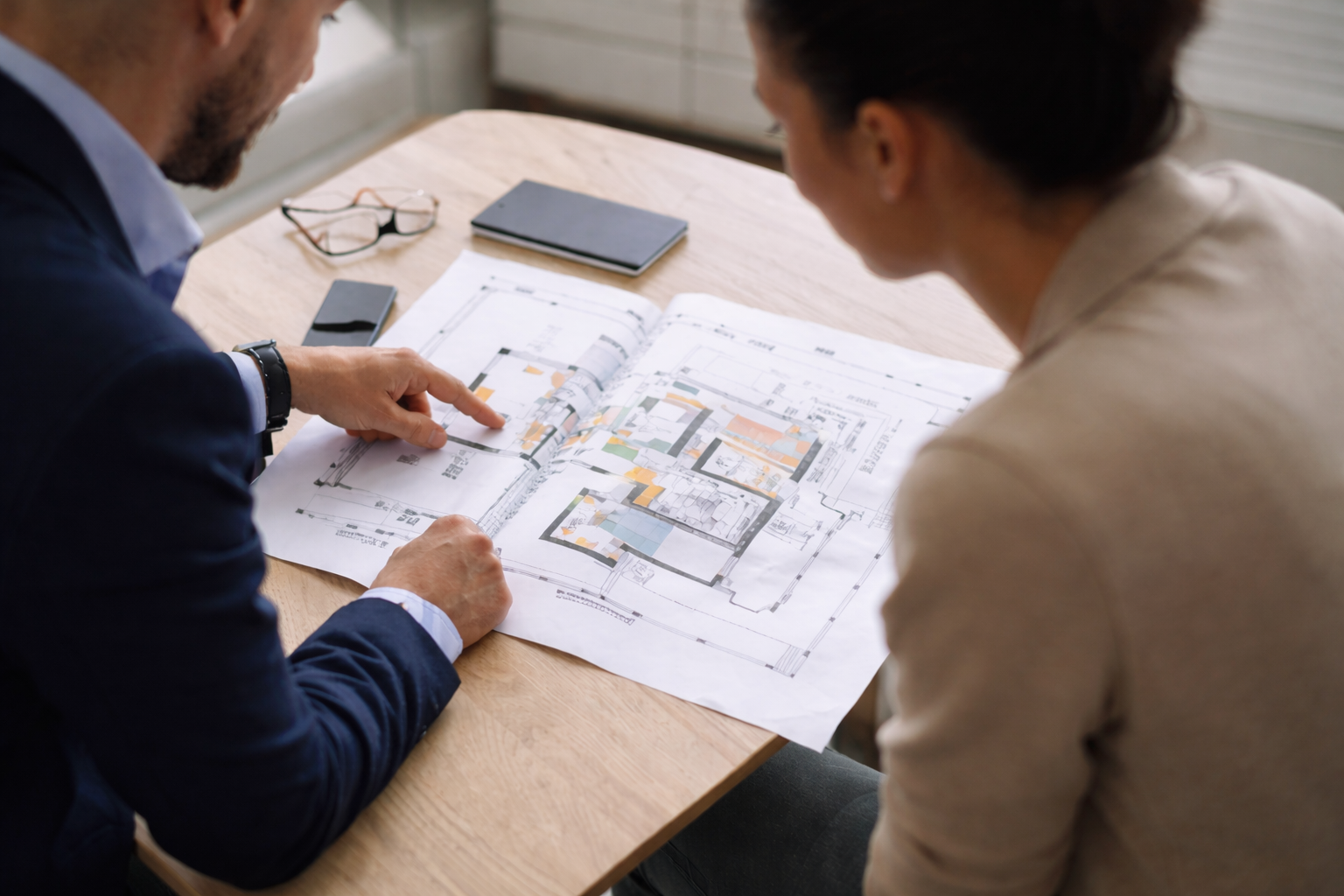 Two professionals reviewing property floor plans together at a desk, pointing at layout details to determine a clear next step in a property transaction